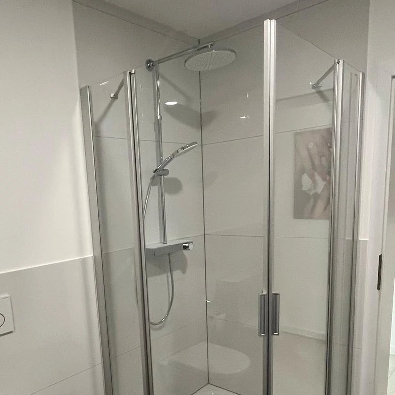 Dusche einbauen: Eckdusche mit zwei Glastüren, Regenbrause und Thermostat-Armatur vor hellgrauen Fliesen
