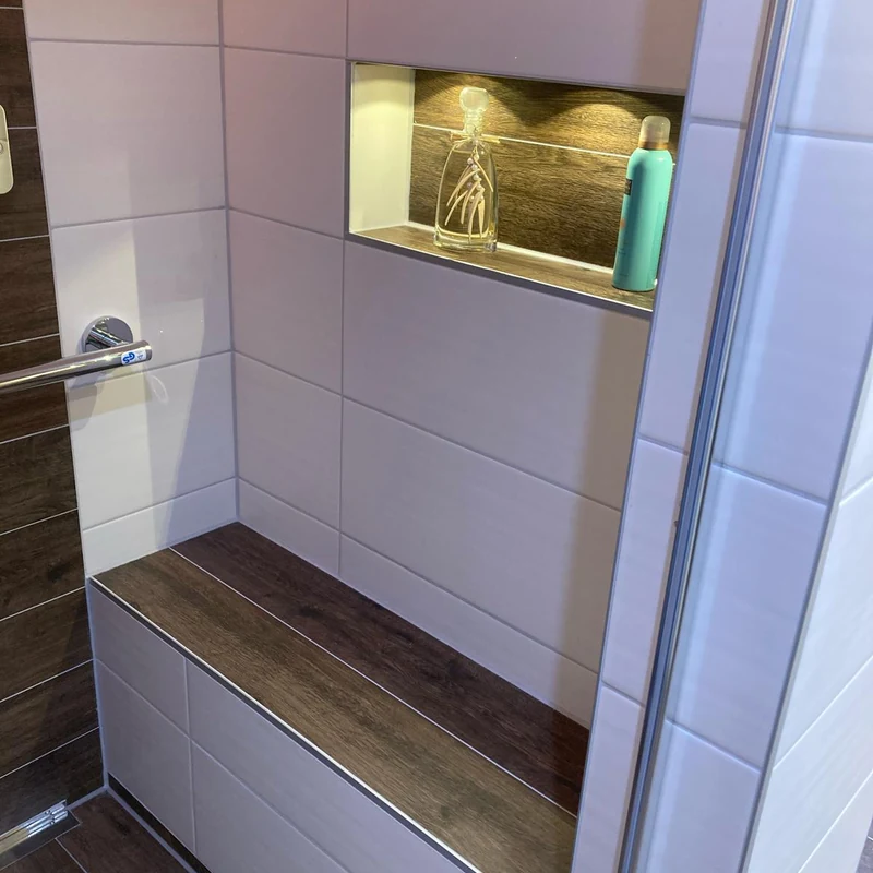 Neue Dusche mit gefliester Sitzbank in Holzoptik, Haltegriff und beleuchteter Nische in einem hellen Bad