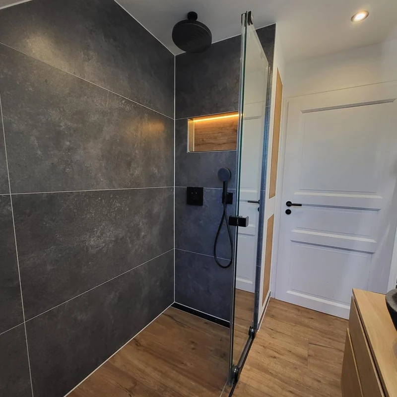Neue Dusche mit Glaswand, Regenbrause und beleuchteter Nische vor dunklen Fliesen